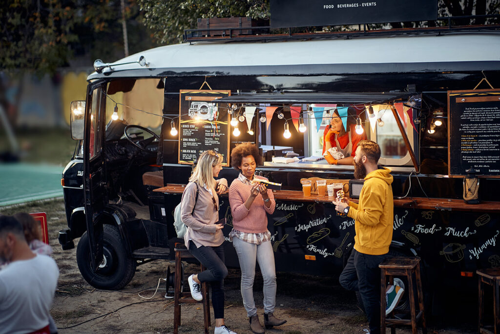 group of friends eating, drinking, talking, socializing outdoor in front of modifed truck for fast food service